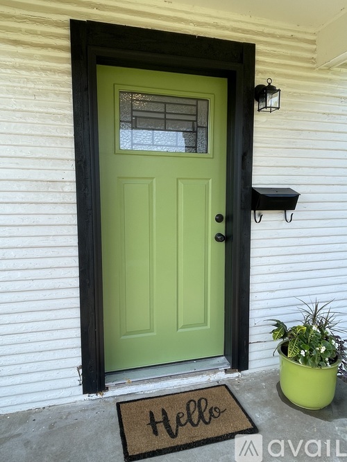 A green door with a black frame and a doormat that says "Hello".