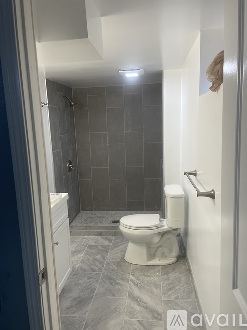 A bathroom with a toilet, tiled walls and floor, and a shower area.