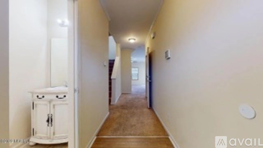 A long hallway with a white cabinet on the left and a door at the end.