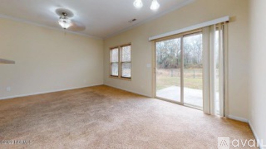 A spacious room with a carpeted floor and sliding glass doors leading to a view of trees.