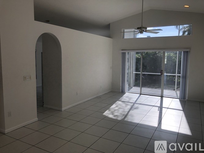 A spacious room with a ceiling fan and sliding glass doors leading to a balcony.