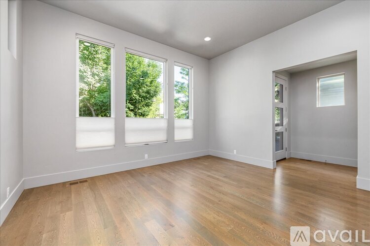 A spacious room with wooden flooring and large windows.