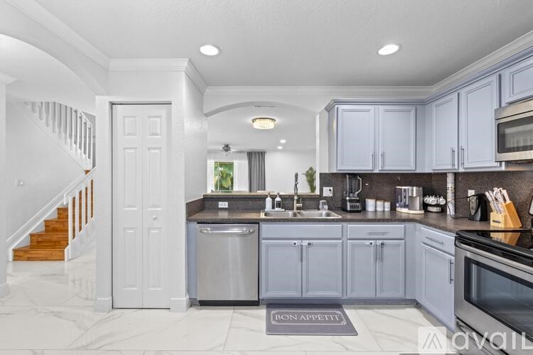 A kitchen with a staircase on the left side and a sink in the middle.