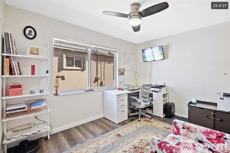 A room with a desk, chair, and a fan.