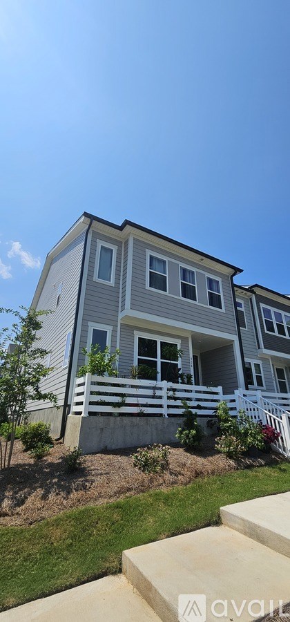 A grey two-story house with a white fence and a small tree in front.