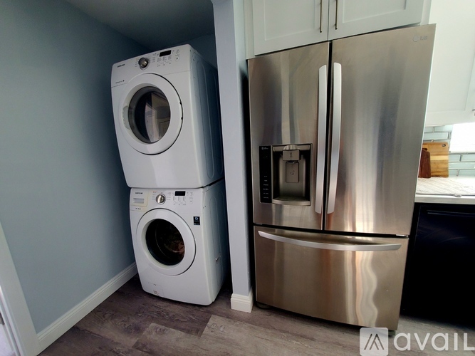A stainless steel refrigerator stands next to a white washing machine in a kitchen.