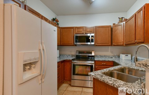 A kitchen with a white refrigerator, wooden cabinets, and a granite countertop.