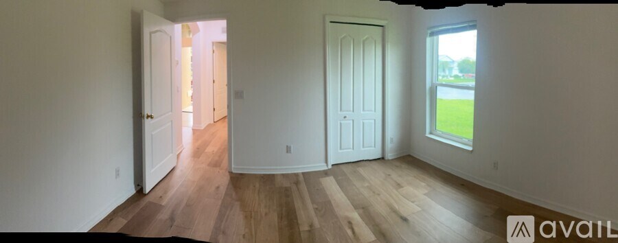 A room with wooden floors and white walls, with a window on the right side.