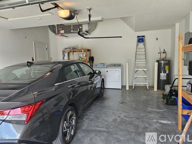 A black car is parked in a garage with a ladder and a white refrigerator.