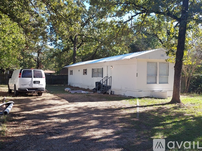 A white house with a blue roof is surrounded by trees and has a white van parked in front.