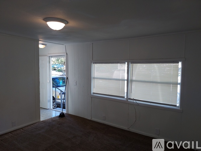 A room with a carpeted floor, a window with blinds, and a door leading to a patio.