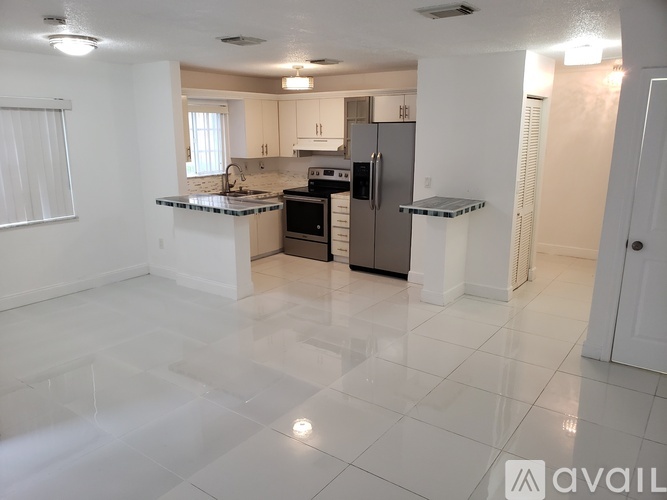 A kitchen with white cabinets and appliances in a large empty room.