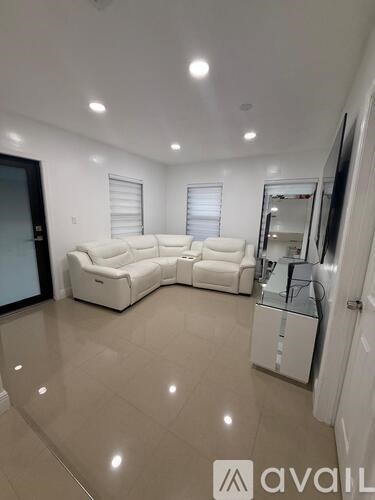 A spacious living room with a white sofa set and a television.