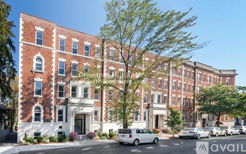 A street view of a red brick building with a tree in front and cars parked on the side of the road.