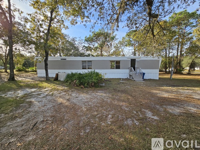 A white mobile home is situated in a grassy area with trees in the background.