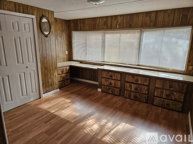 A room with wooden walls and floor, a white door, and a window with blinds.