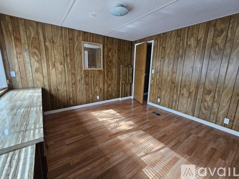 A room with wooden walls and flooring, a door, and a window with blinds.