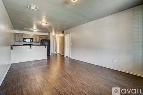 A room with wooden floors and a kitchenette in the corner.