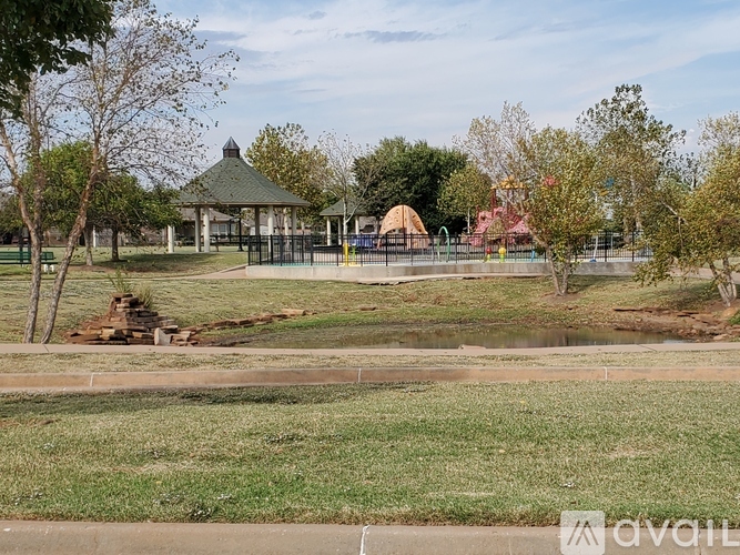 A gazebo sits in the middle of a park with a playground in the background.