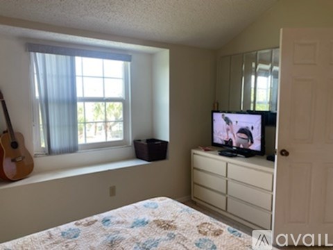 A bedroom with a bed, a window with a guitar on the windowsill, a dresser with a TV on top, and a door.