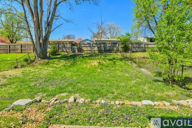 A backyard with a fence, trees, and a flower bed.