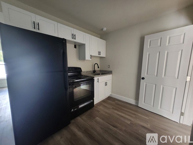 A kitchen with a black fridge, white cabinets, and a white door.