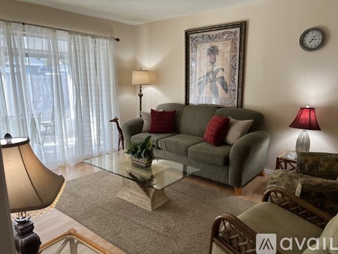 A living room with a grey couch, a glass coffee table, and a painting on the wall.