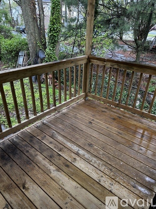 A wooden deck with a railing and a view of trees and a house in the background.