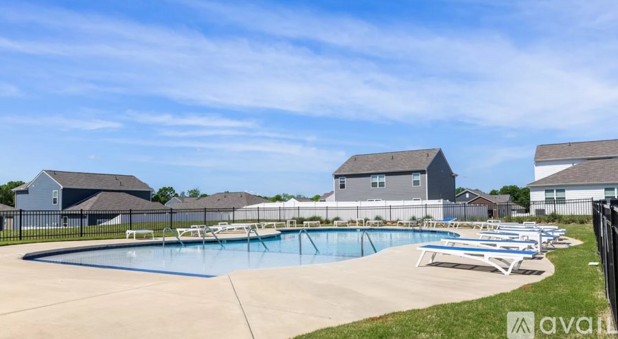A large swimming pool surrounded by lounge chairs and a fence with the Avail apartments logo in the background.