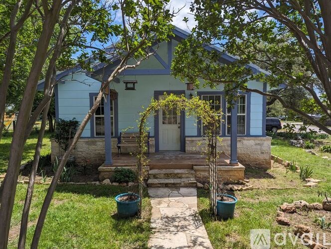 A blue house with a front porch and a tree in front.