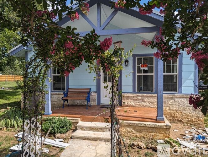 A blue house with a porch and a bench under a tree.