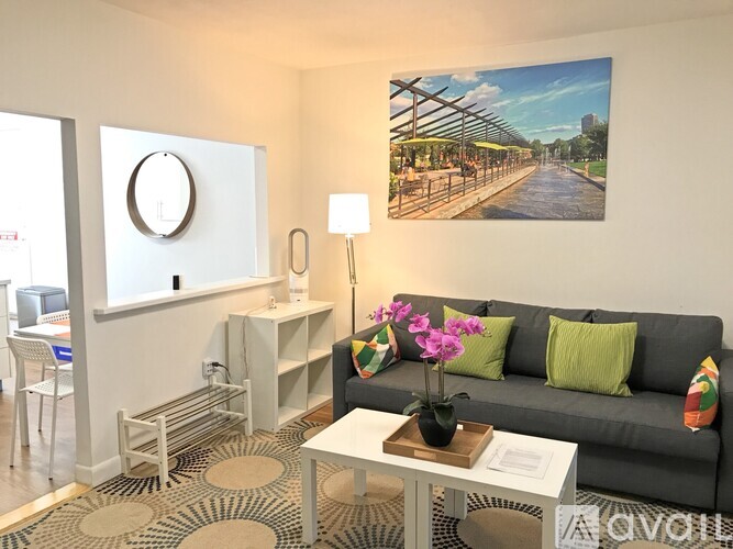 A living room with a grey couch, a white coffee table, and a painting of a bridge on the wall.