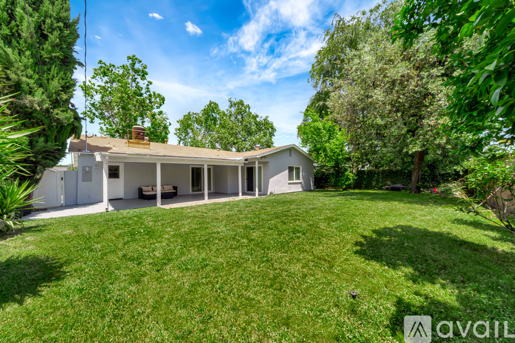 A house with a large lawn and trees in the background is for sale.