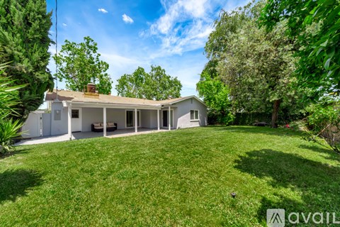 A house with a large lawn and trees in the background is for sale.