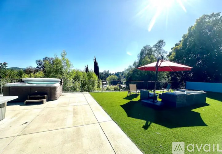 A sunny day in a backyard with a hot tub and a red umbrella.