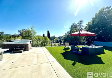 A sunny day in a backyard with a hot tub and a red umbrella.