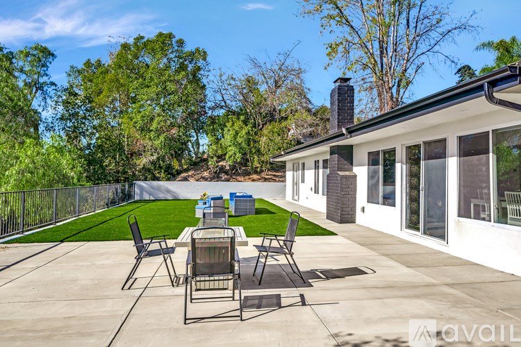 A patio with a table and chairs is surrounded by a green lawn and trees.