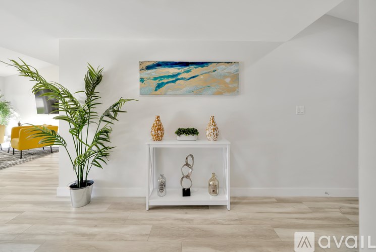 A living room with a white shelf, a potted plant, and a painting on the wall.