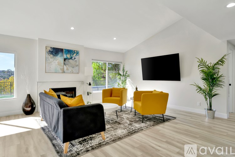 A living room with a black couch, yellow chairs, and a flat screen TV mounted on the wall.