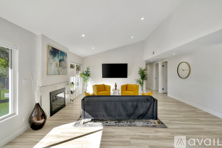 A modern living room with a grey sofa, a yellow chair, a fireplace, and a TV mounted on the wall.