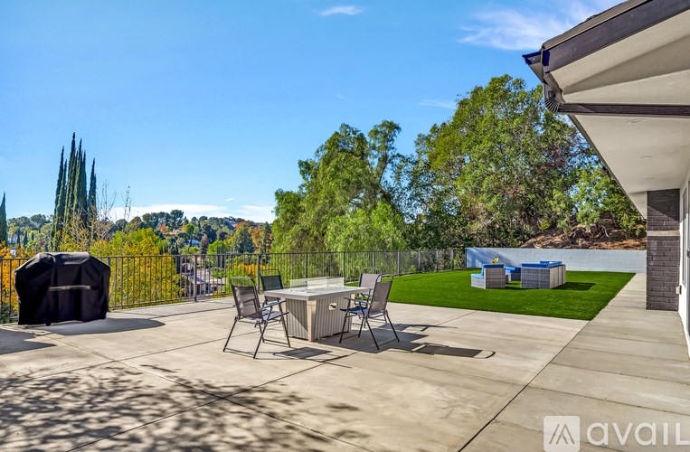 A patio with chairs and a hot tub is surrounded by trees.