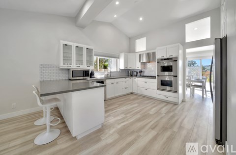 A modern kitchen with white cabinets and a wooden floor.