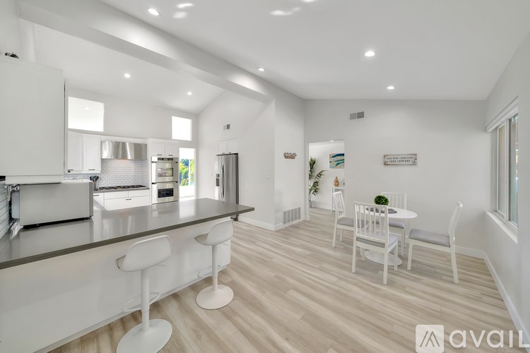 A modern kitchen with white furniture and a dining area.