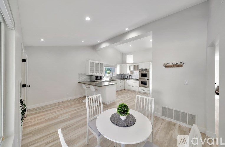 A white table with a plant on it is in the middle of a kitchen and dining area.