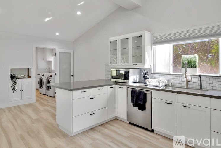 A modern kitchen with white cabinets and a wooden floor.