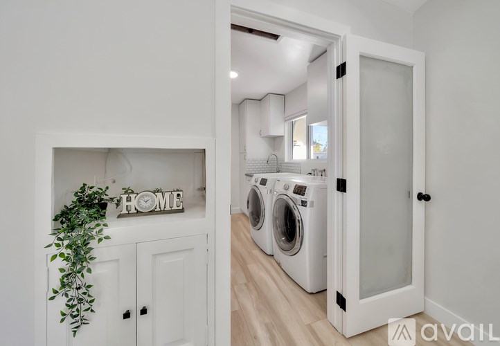 A white laundry room with a sign that says "HOME" and a plant on the left.