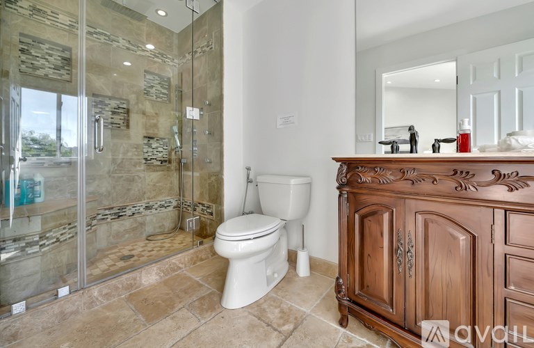 A bathroom with a toilet, a wooden cabinet, and a glass shower stall.