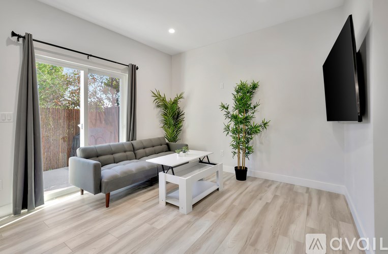 A living room with a grey couch, a white coffee table, and a flat screen TV mounted on the wall.