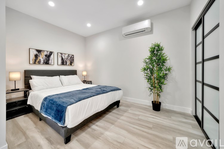 A bedroom with a bed, a potted plant, and two framed pictures on the wall.