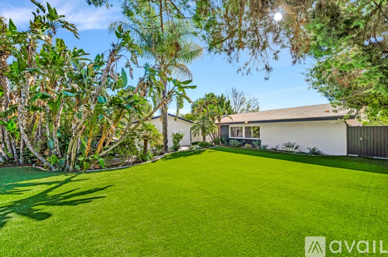 A well-maintained lawn leads to a white house with a brown roof.